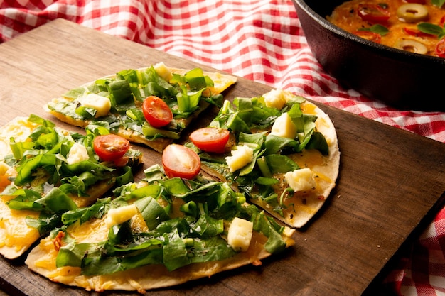 Pizza hecha a mano de rúcula servida en una tabla de corte de madera sobre una mesa de madera con un paño de picnic rojo