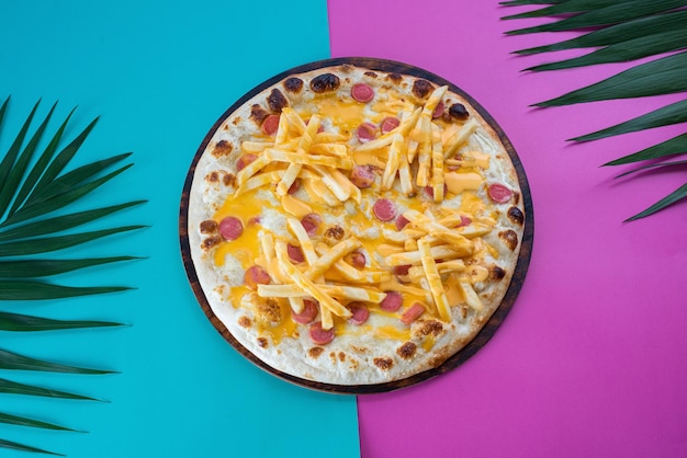 Pizza infantil com batatas fritas e salsicha em um fundo colorido azul e roxo vista superior