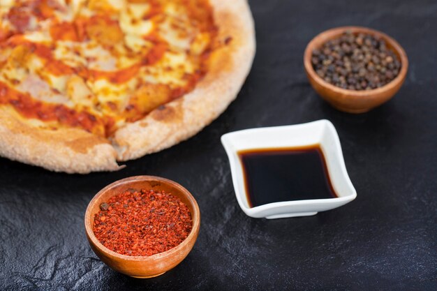 Pizza inteira com especiarias e molho de soja colocada na mesa preta.