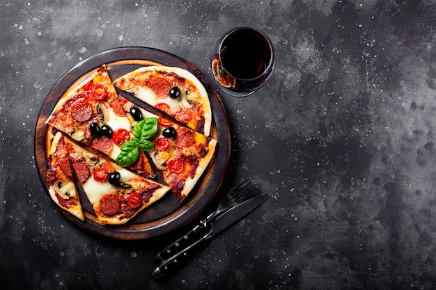 Pizza italiana caseira com mussarela, linguiça calabresa, azeitonas e manjericão e uma taça de vinho tinto