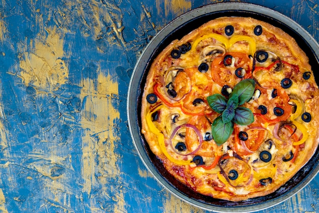 Pizza italiana casera caliente con albahaca, aceitunas, tomates, jamón y queso. Espacio libre para texto