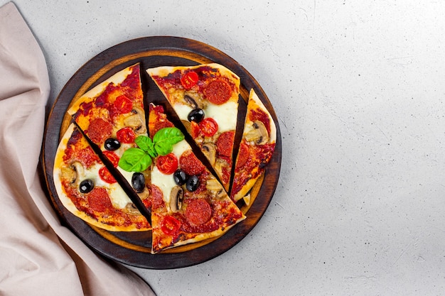 Foto pizza italiana casera fresca con mozzarella, salchichas de pepperoni, aceitunas y albahaca en la vista superior de la tabla de cortar