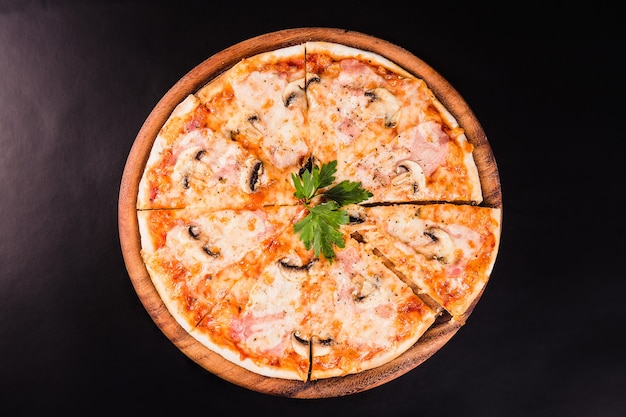 Pizza italiana com cogumelos em uma placa de madeira em um fundo preto