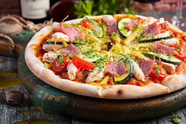 Pizza italiana com frango, salame, abobrinha, tomates e ervas em fundo de madeira vintage