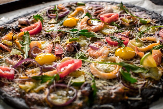 Pizza italiana com massa preta e frutos do mar em uma assadeira saindo do forno. Em cima dele, havia lulas, camarões, polvos, cebolas, tomates. Tinta de choco