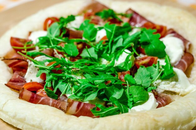 Foto pizza italiana com queijo mussarela, tomate, bacon e rúcula fresca na mesa de madeira.