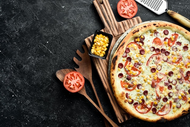 Pizza italiana com salsichas, milho e queijo, comida para levar sobre um fundo de pedra preta, estilo rústico.