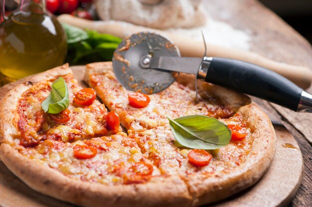 Pizza italiana com tomate coberto com queijo dourado derretido, ervas e manjericão servida em uma tábua redonda de madeira sobre uma velha mesa de madeira