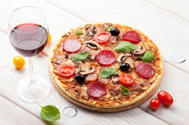 Pizza italiana com tomates pepperoni azeitonas manjericão e vinho tinto