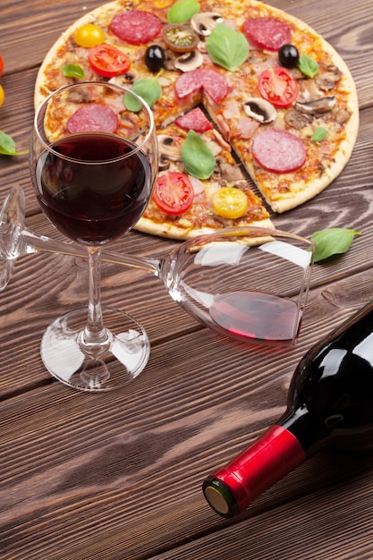 Foto pizza italiana com tomates pepperoni azeitonas manjericão e vinho tinto