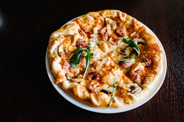 Pizza italiana de carne com rúcula em mesa de madeira marrom