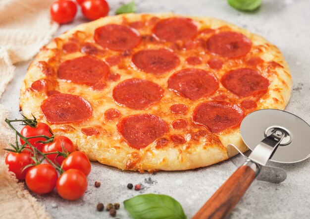 Pizza italiana de pepperoni assada na hora com cortador de rodas, tomate e manjericão