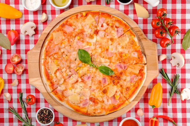 Foto pizza italiana havaiana com queijo parmesão, abacaxi, milho, coberturas de presunto, manjericão fresco e molho de tomate em uma placa de madeira