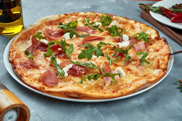 Pizza italiana con jamón, rúcula y queso crema sobre un gris