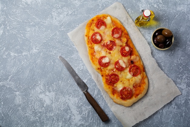 Pizza italiana ovalada con tomate Margarita sobre hormigón gris.