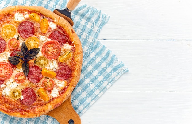 Pizza italiana de pepperoni con salami y queso sobre fondo blanco de madera rústica