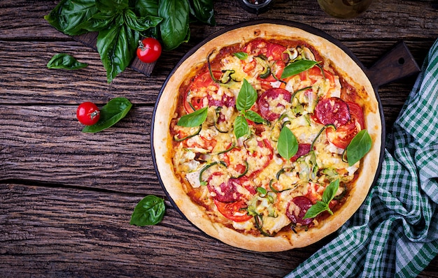 Pizza italiana con pollo, salami, calabacín, tomates y hierbas sobre fondo de madera vintage. Vista superior. cocina italiana