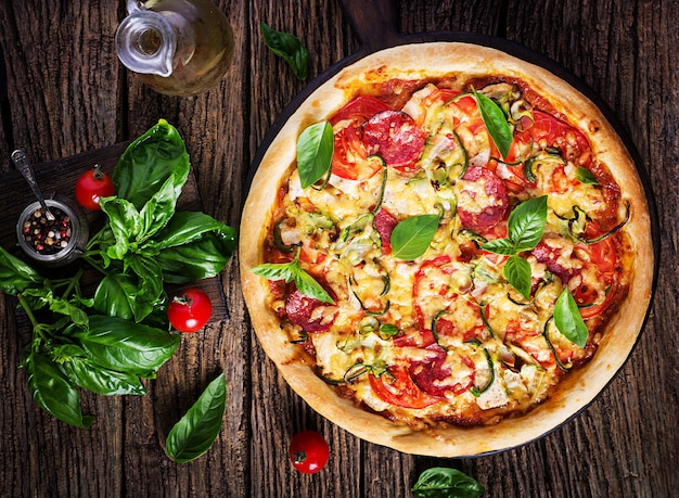 Foto pizza italiana con pollo, salami, calabacín, tomates y hierbas.