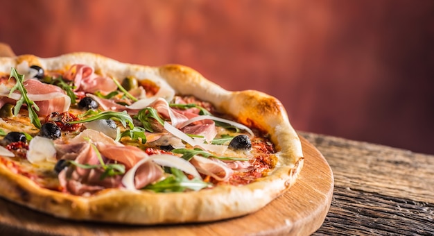 Pizza italiana con prosciutto tomates aceitunas aceite de oliva queso parmesano y rúcula