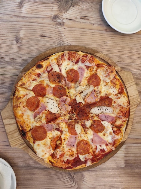 Pizza italiana con salchichas de queso mozzarella derretida rebanadas de tocino en una corteza gruesa en un plato de madera y una mesa de madera en un café