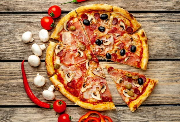 Pizza italiana con tocino, champiñones, aceitunas, tomates sobre un fondo de madera