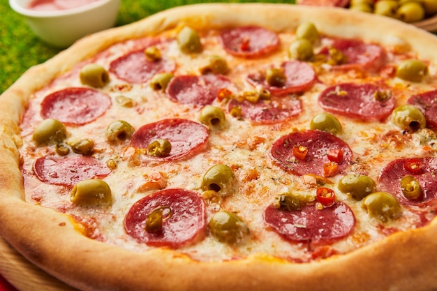 Pizza italiana tradicional de pepperoni com salame, mussarela, azeitonas e manjericão na grama verde