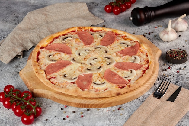 Pizza con jamón y champiñones, tablero de madera, fondo gris