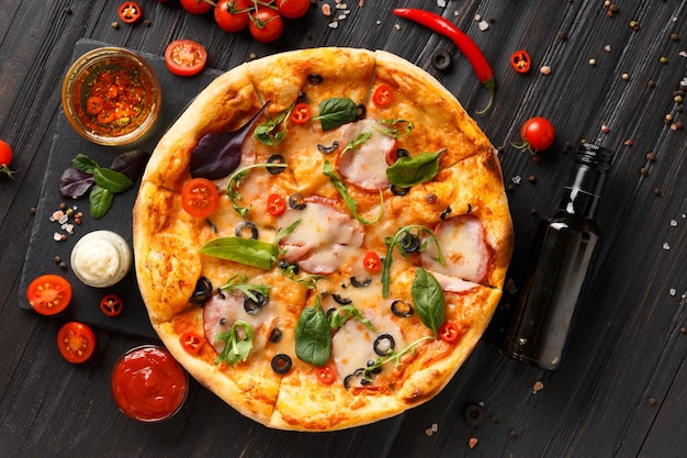 Foto pizza con jamón en un plato de piedra negra sobre un fondo de madera oscura vista superior