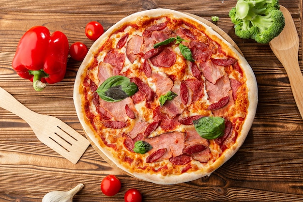 Pizza con jamón, salchichas calientes, salami y mozzarella sobre fondo de madera de cerca. Cocina italiana. Pizza con jamón y salami en mesa de madera. vista superior.