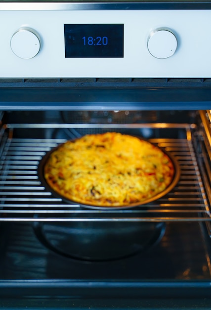 Pizza kochen auf einem runden Tablett in einem Gasofen. Pizza mit Käse auf einem runden Blech im Ofen. Hausgemacht.