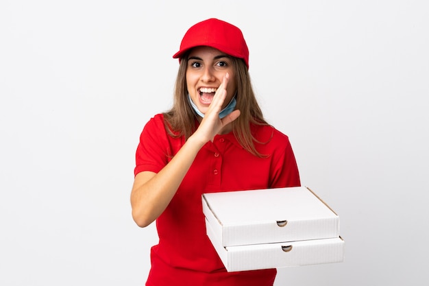 Pizza-Lieferfrau, die eine Pizza hält und vor dem Coronavirus mit einer Maske auf isolierter weißer Wand schützt, die etwas flüstert