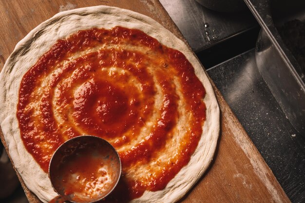 Pizza machen. Soße hinzufügen. Koch bereitet italienische Pizza zu