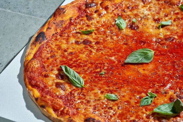 Pizza margarita com molho de tomate, tomate, manjericão e guarnições crocantes. Luz forte. Superfície cinzenta. Close up, foco seletivo