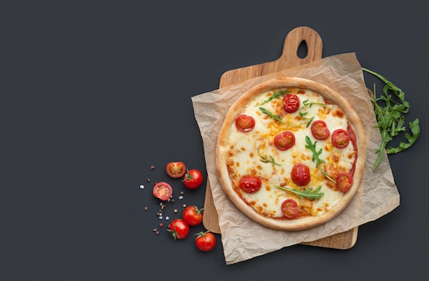 pizza margarita en una tabla con ingredientes en un fondo negro