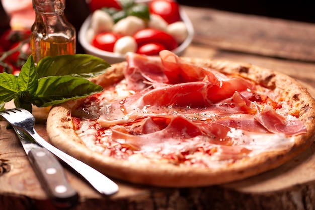 Pizza margherita con jamón de Parma sobre una mesa rústica