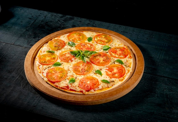 Pizza Margherita mit Käse, Basilikum und Tomaten auf indigoblauem Holztisch.
