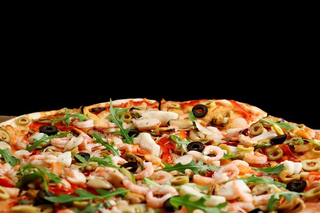 Pizza con mariscos pimiento rojo y aceitunas sobre fondo negro de cerca