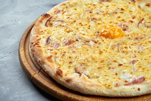 Pizza mit Eigelb, Parmesan, Speck und cremiger Sauce auf einem Holztablett