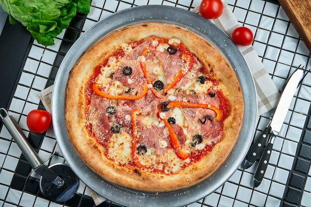 Pizza mit einer großen Anzahl von Belägen: Salami, Paprika, Oliven, Käse. Pizza in Zusammensetzung mit Zutaten auf einem weißen Tisch. Essen flach lag