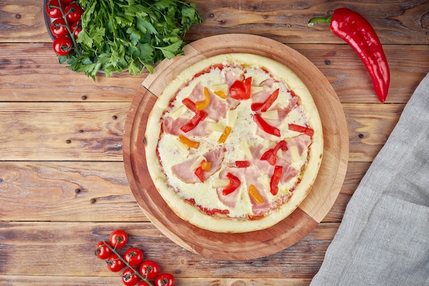 Pizza mit Fleisch, Gemüse und Pilzen, hölzerner Hintergrund