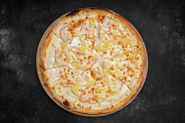 Pizza mit Fleischschinkenananas auf einem runden Holzbrett auf grauer Betondraufsicht