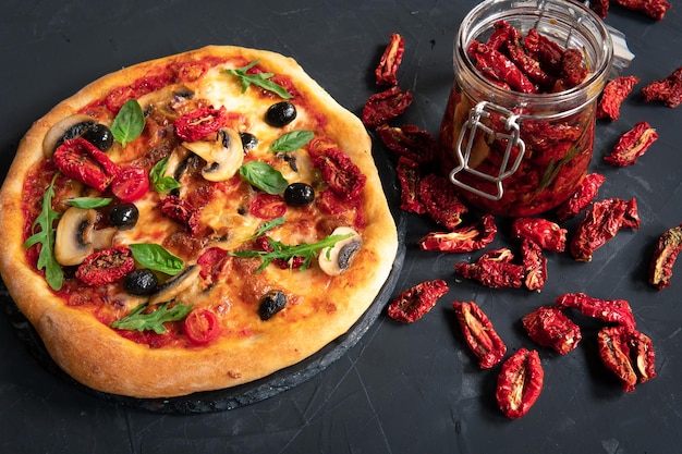 Pizza mit Gemüse und getrockneten Tomaten auf dunklem Hintergrund in der Küche