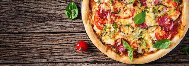 Pizza mit Huhn, Salami, Zucchini, Tomaten und Kräutern auf Weinleseholztisch. . Banner. italienische Küche