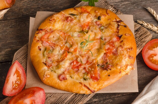 Pizza mit Käse und Tomaten auf einer hölzernen Hintergrundnahaufnahme mit Zutaten