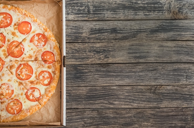 Pizza mit Käse und Tomaten in einer Box mit Kopienraum auf einem dunklen hölzernen Hintergrund.