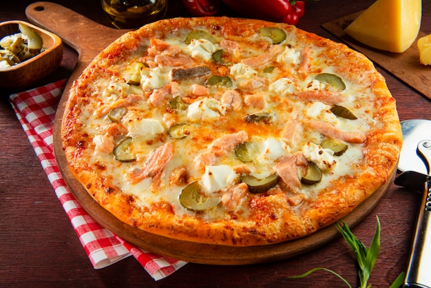 Pizza mit Lachs und Käse auf einem Holztisch mit Zutaten