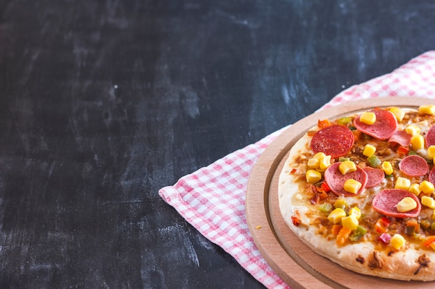 Pizza mit Mais, Wurst, Tomaten auf einem hölzernen runden Brett