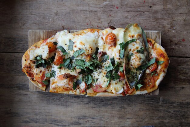 Pizza mit Meeresfrüchten und Tomaten auf einem Holztisch, italienisches Essen