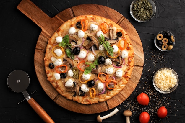 Pizza mit Mozzarella, Oliven und Pilzen. Italienische Küche. Zutaten für die Herstellung von Pizza auf einem schwarzen Hintergrund. Draufsicht. Konzept für die Werbung für Restaurants.