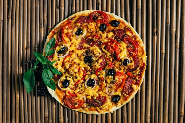 Pizza mit Oliven und Salami, dekoriert mit Beeren und Basilikum